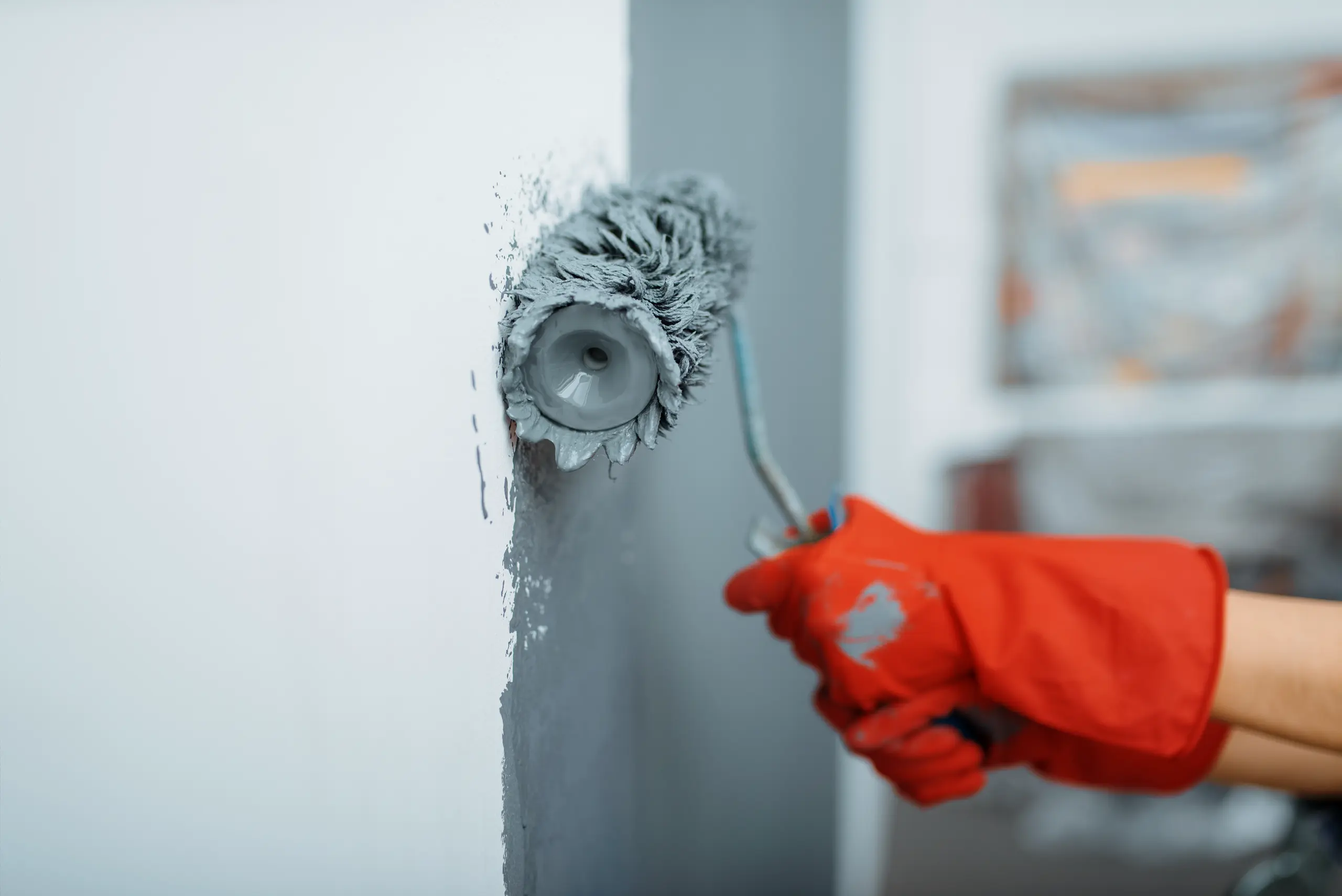 A person in red gloves painting a wall with a gray roller
