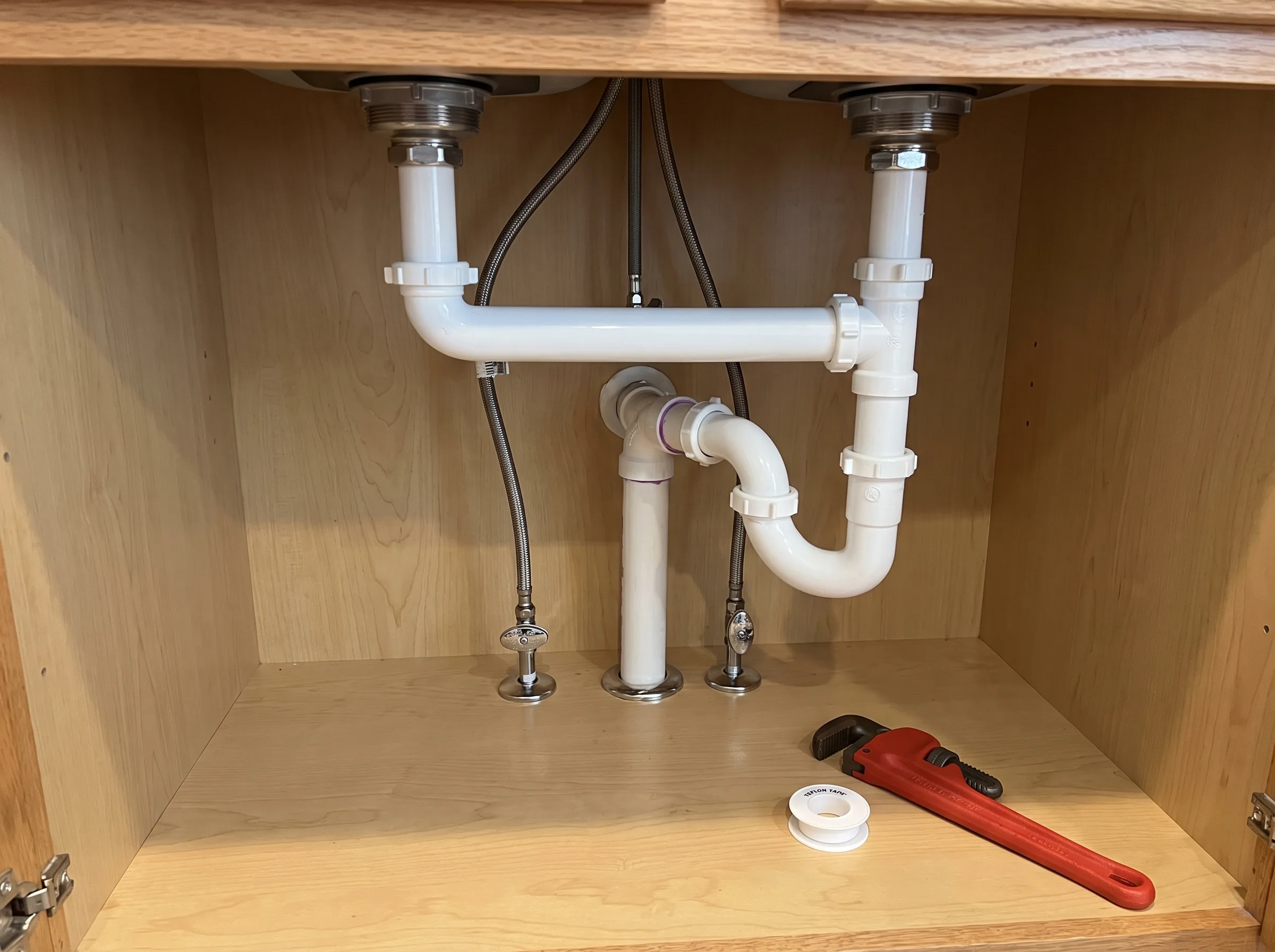 Under-sink plumbing installation showing pipes and a wrench for adjustments